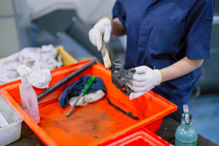 Un trabajador de una planta industrial limpia varias piezas a mano.